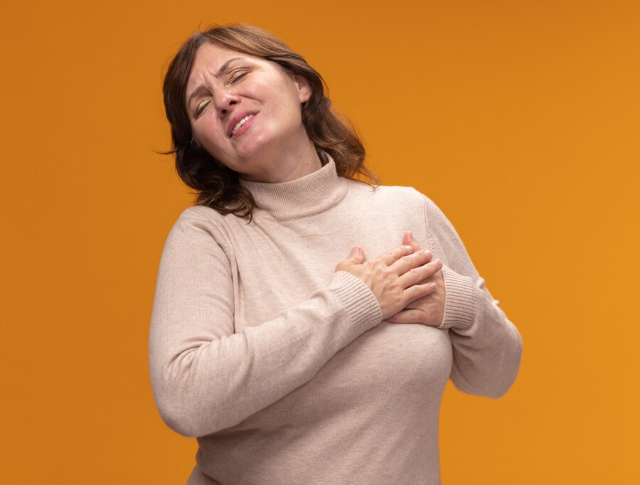 middle aged woman beige turtleneck holding hand her chest feeling thankful with closed eyes standing orange wall 141793 81825 یائسگی و پوکی استخوان، مفاصل، و ناراحتی‌های قلبی | راهنمای کامل مدبی